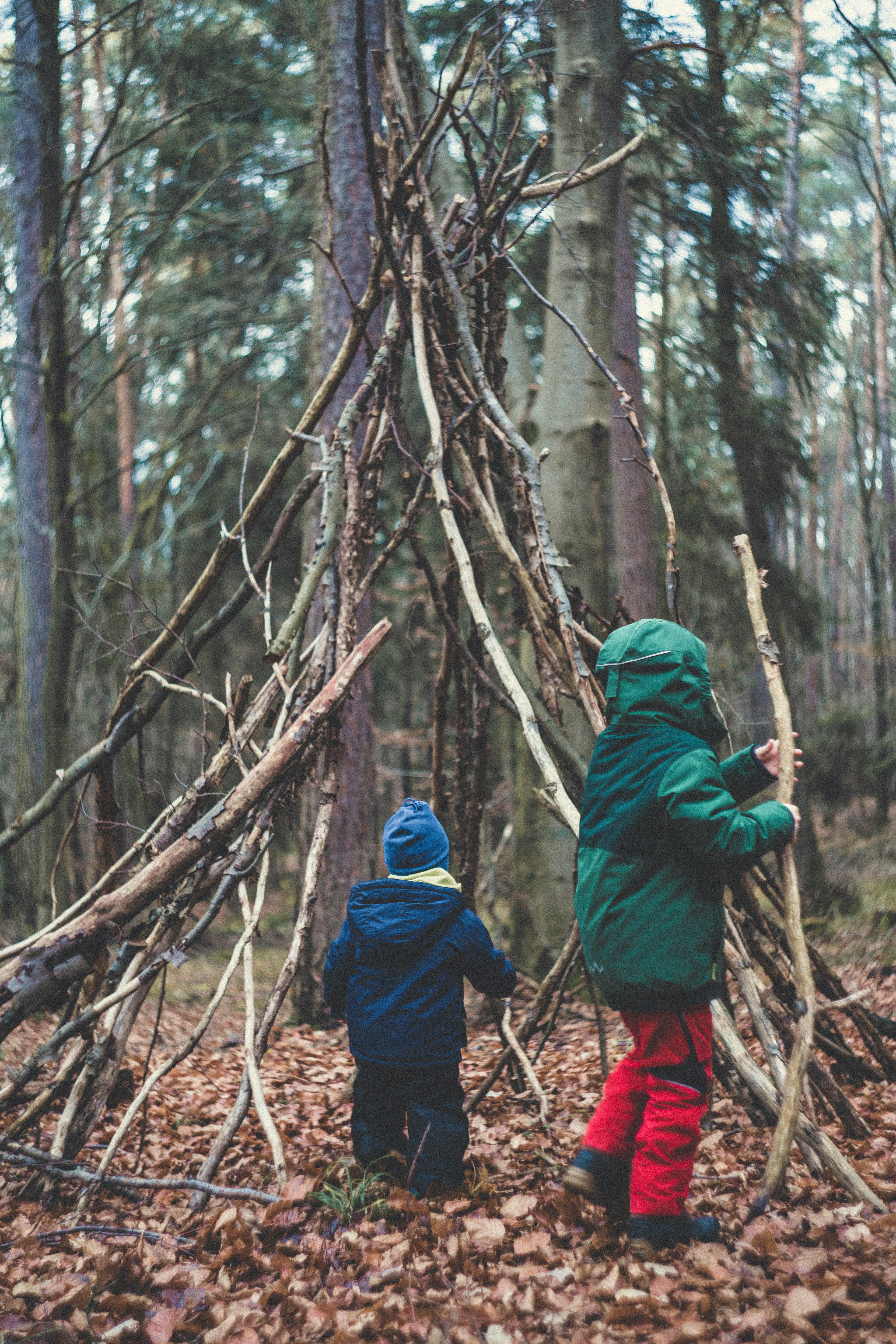 two children building fort from large branches in forest-markus-spiske-unsplash
